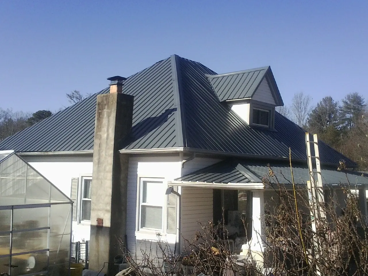 Dark blue standing seam metal roof on a white farmhouse with dormer — Slate & Tile Roof Repair by Roofing Brothers in Karthaus