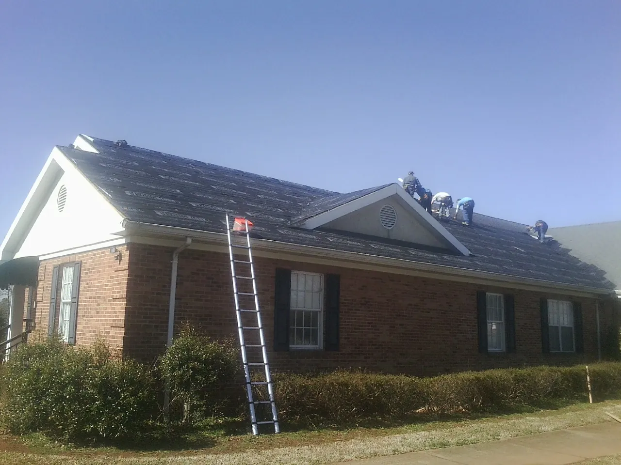 Crew tearing shingles off a brick ranch roof with a ladder set — Metal Roof Repair work by our crew in Karthaus