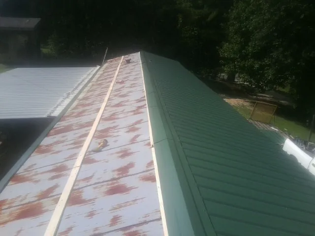 Old rusted panels beside newly installed green metal roofing — Wind Damage Roof Repair by Roofing Brothers in Karthaus