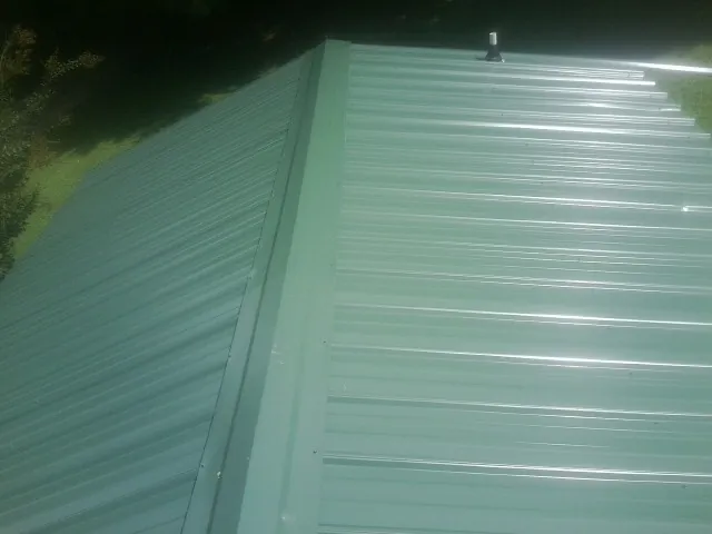 New green metal panels meeting at the ridge of a roof — Flat Roof Repair work by our crew in Karthaus