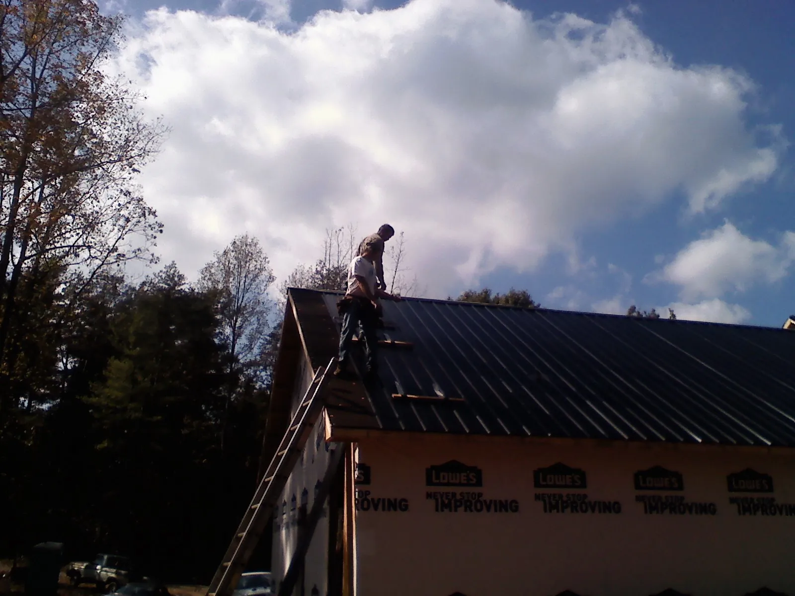 Roofer fastening dark metal panels high against a cloudy sky, from a Roof Inspection job in Karthaus