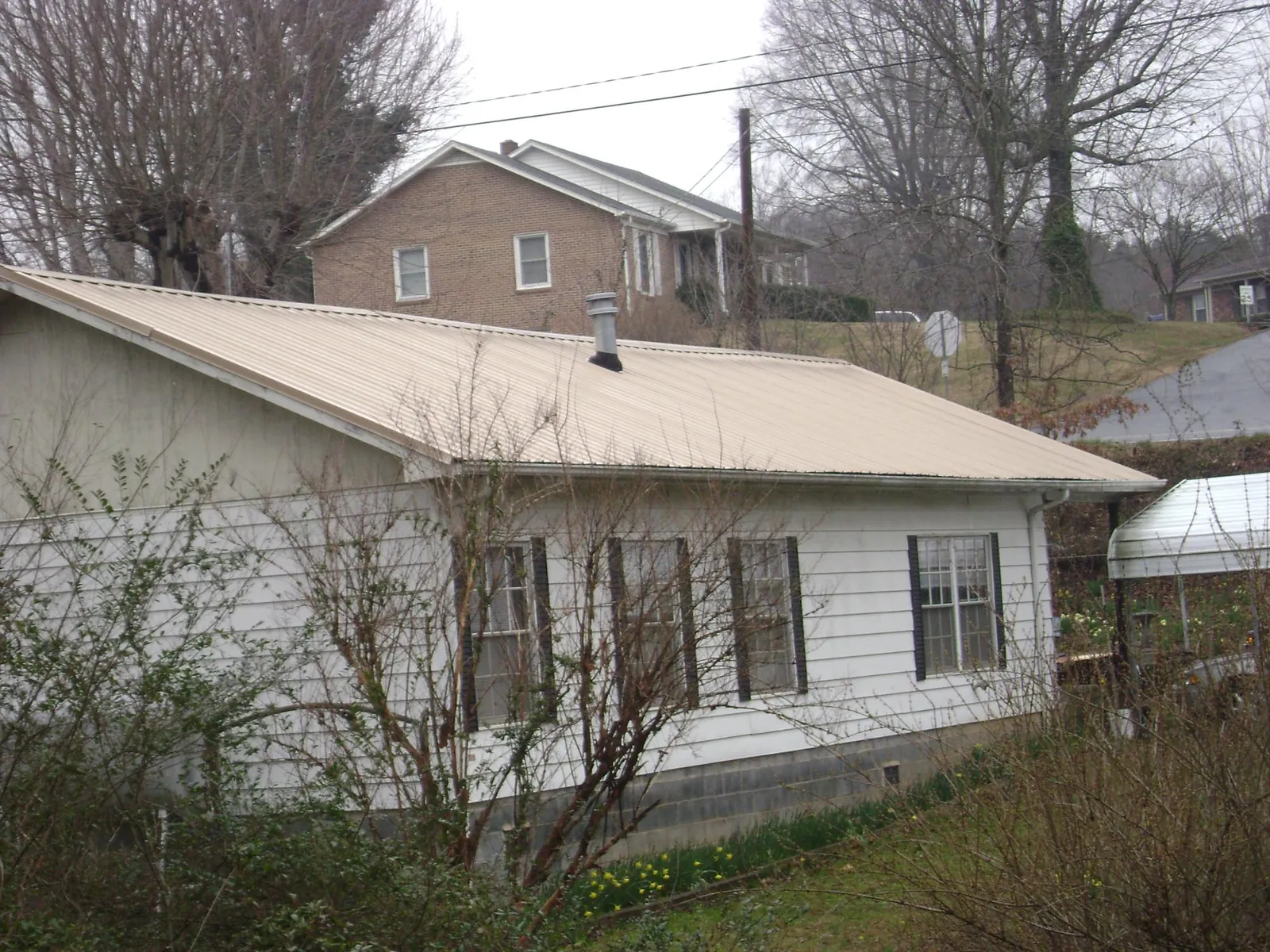 Tan metal roof on a white sided house set into a hillside — Commercial Roofing by Roofing Brothers in Karthaus